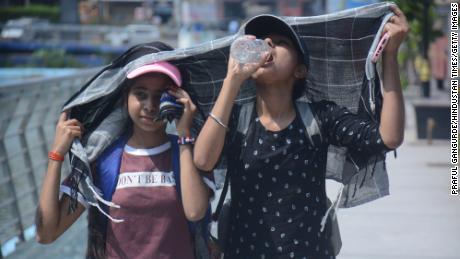 Mädchen bedecken ihre Köpfe, während sie in der sengenden Nachmittagshitze von Mumbai spazieren gehen und Wasser trinken.