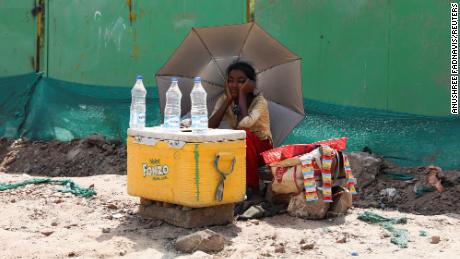 Ein Mädchen, das Wasser verkauft, benutzt einen Regenschirm, um sich in Neu-Delhi vor den Sonnenstrahlen zu schützen.