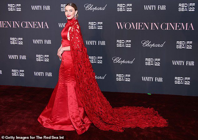 ATEMBERAUBENDES CAPE: Das rote Kleid zeigte einen langen, gekräuselten Umhang, der während eines Fotoshootings auf dem roten Teppich in einer langen Schleppe hinter ihr herabfloss
